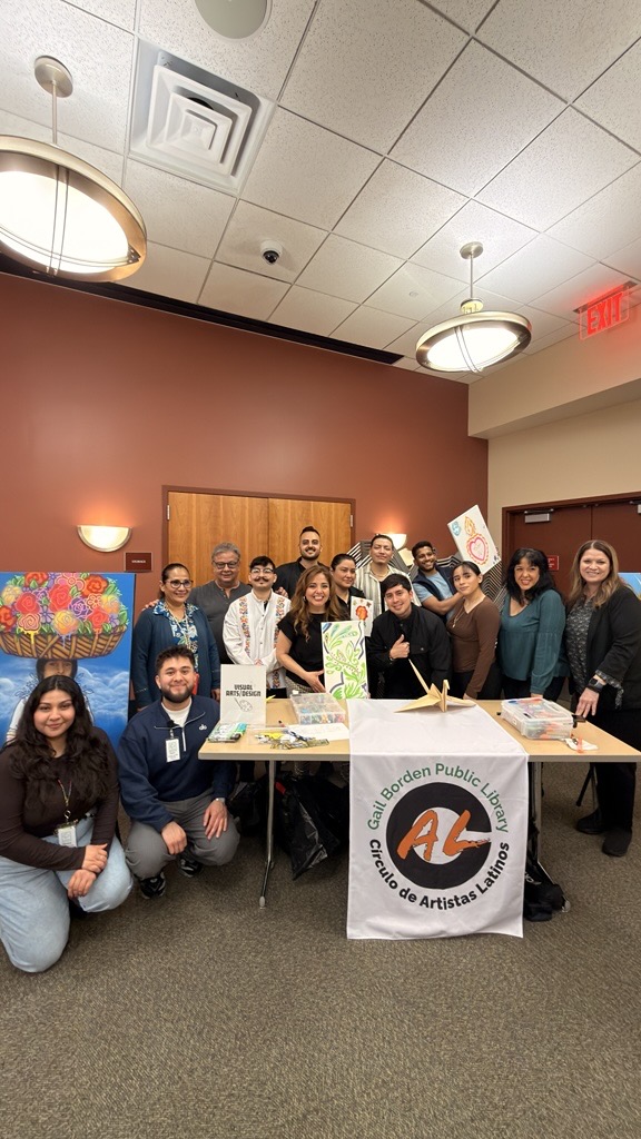 Community members and library staff pose behind a display table featuring artwork, art supplies, and a banner for the Círculo de Artistas Latinos, highlighting a community arts program and exhibition.